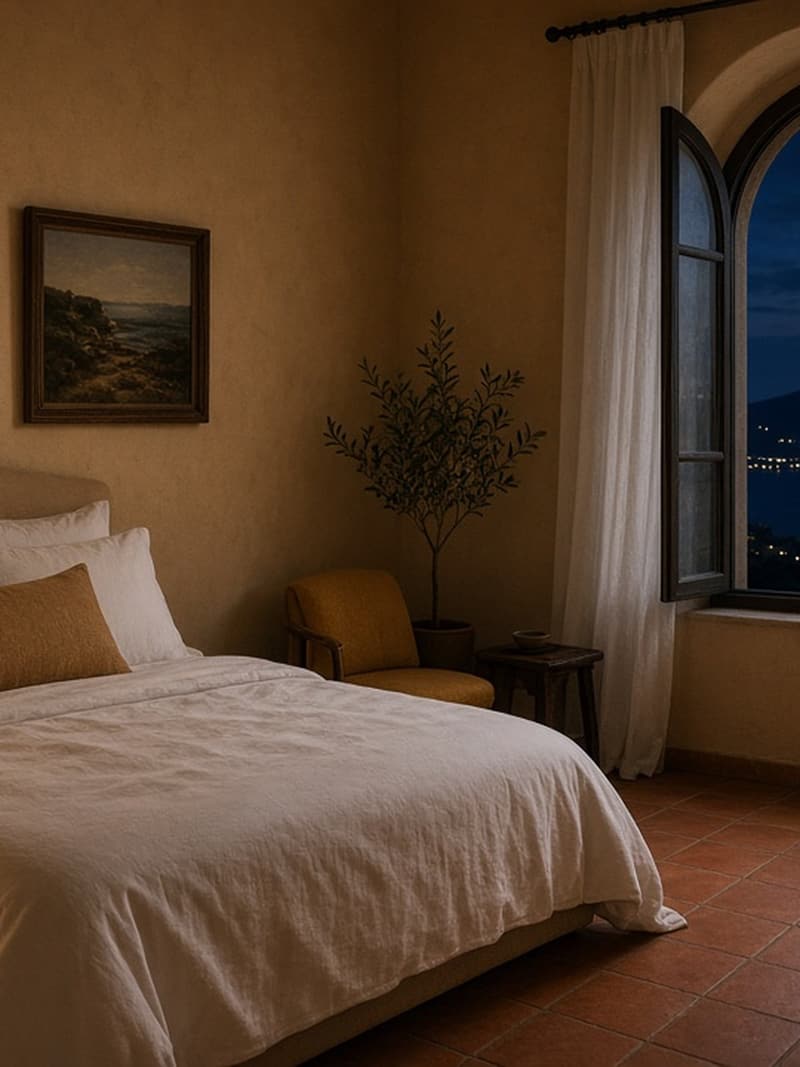 A warm stone bedroom with white linen and an arched window to the sea